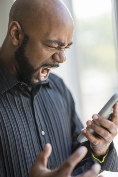 Frustrated black man using cell phone near window