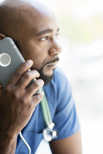 Black nurse talking on cell phone near window