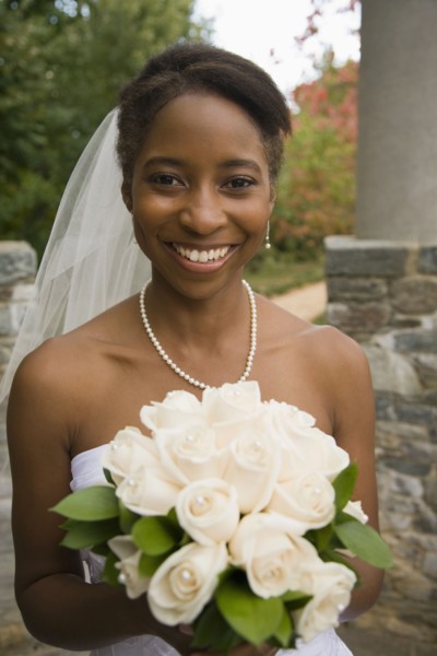 African bride holding rose bouquet and smiling