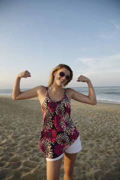 Smiling Caucasian teenage girl flexing biceps on beach
