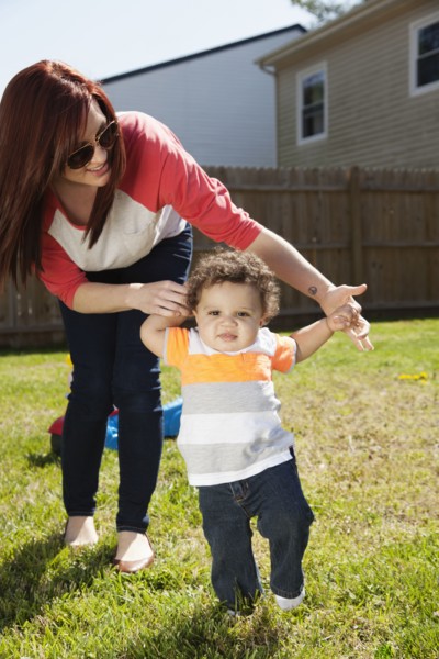 Mother helping baby walk in backyard