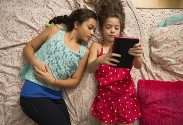 Mixed race sisters using digital tablet on bed