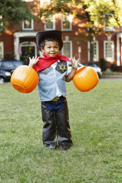 Mixed race boy in cowboy costume holding pumpkin pails on Halloween