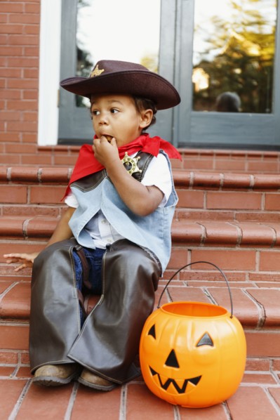 Mixed race boy dressed as cowboy eating Halloween candy