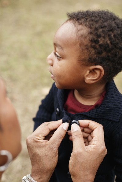 African American mother buttoning sweater of son