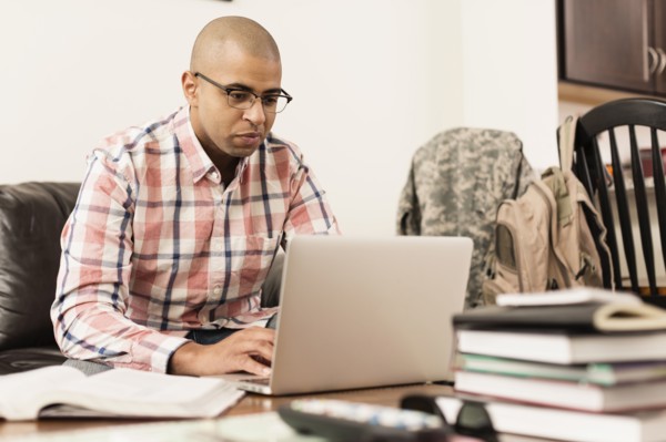 Mixed race soldier using laptop on living room sofa