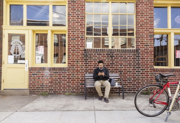 Hispanic man sitting on city bench using cell phone