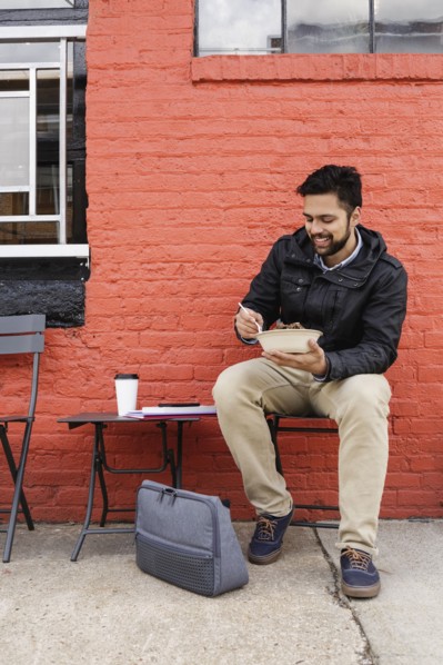 Hispanic man eating bowl of food on sidewalk