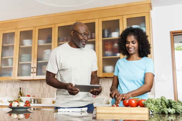 Black couple with digital tablet chopping tomatoes in kitchen
