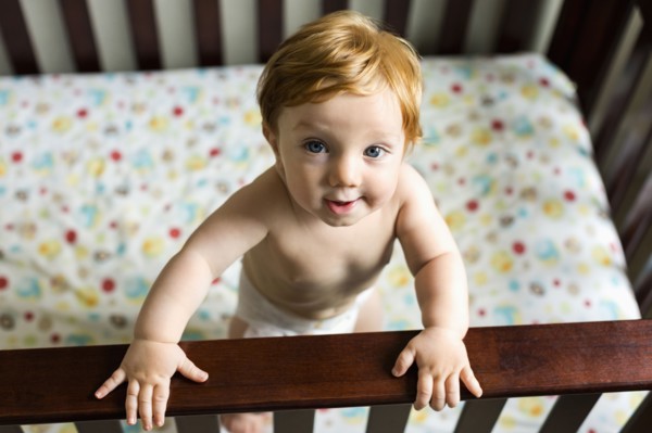 Portrait of curious Caucasian baby boy standing in crib