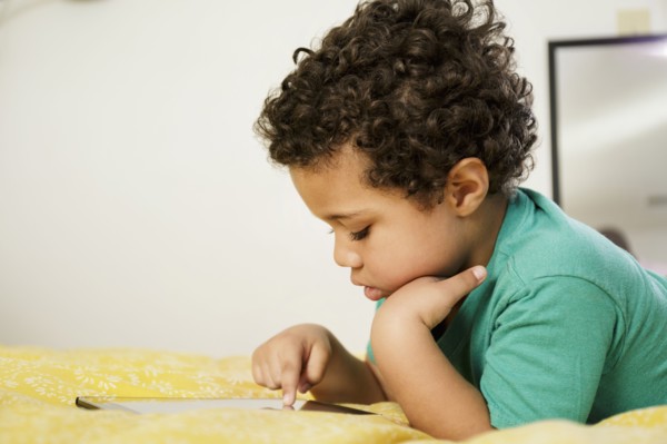 Mixed Race boy laying on bed using digital tablet