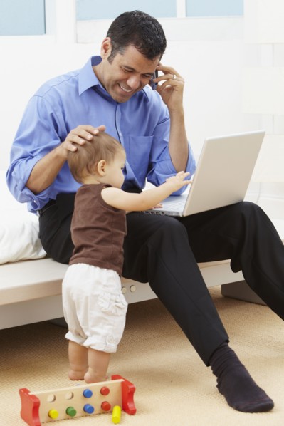 Hispanic father watching daughter and using laptop
