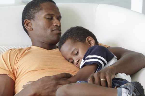 African American father napping on sofa with son