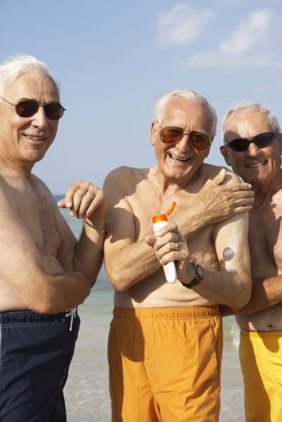 Senior men applying sunscreen on beach