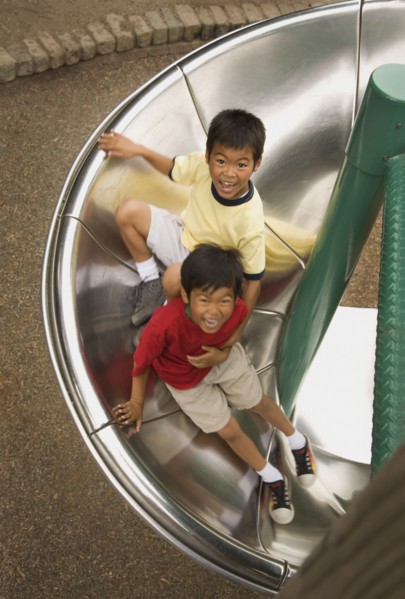 Asian boys sliding down circular slide