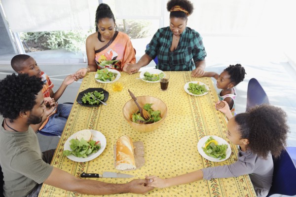Black family saying grace at dining room table