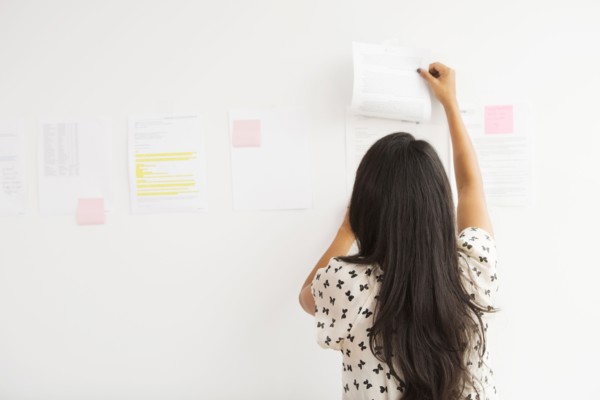 Businesswoman taping up papers on office wall