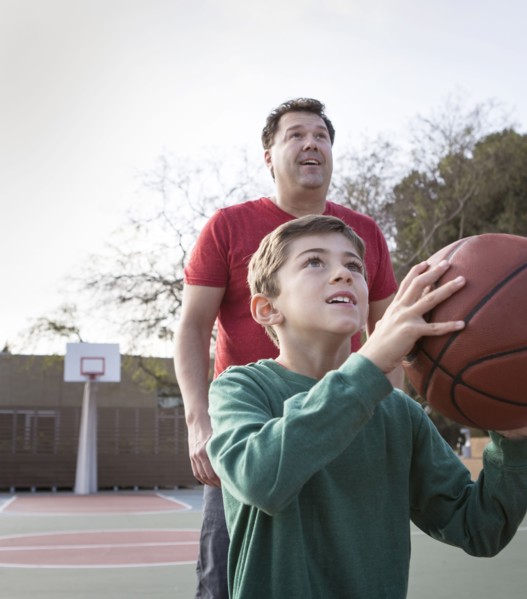 Caucasian father watching son hold basketball on court