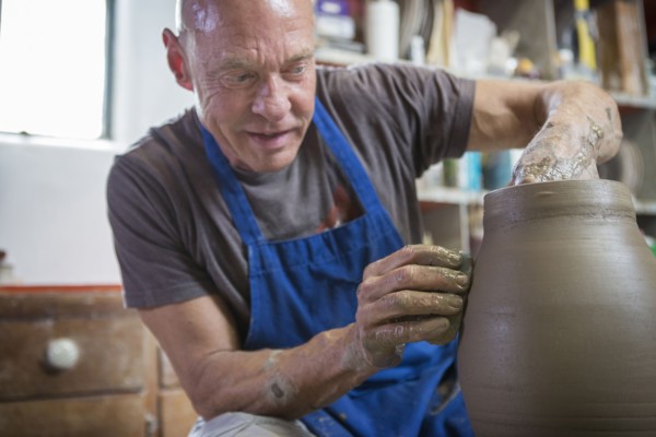 Older Caucasian man forming pottery on wheel in ceramics studio