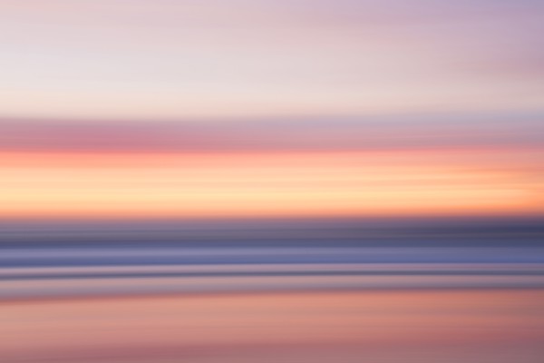 Defocused view of ocean waves on beach under sunset sky