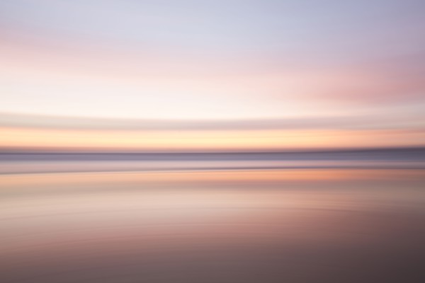 Defocused view of ocean waves on beach under sunset sky