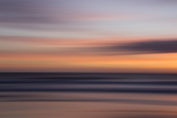 Defocused view of ocean waves on beach under sunset sky