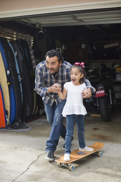 Hispanic father teaching daughter to ride skateboard