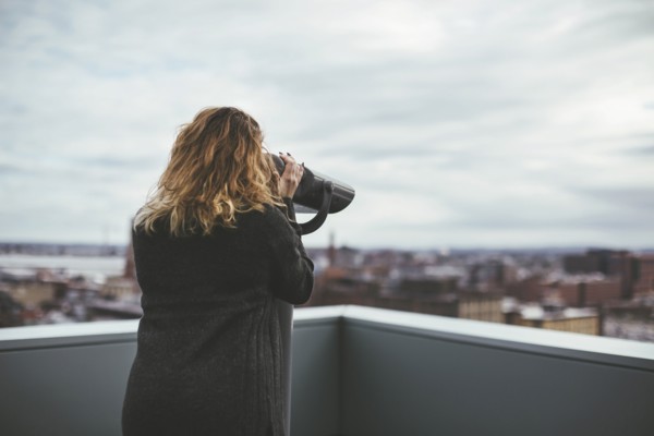 Caucasian woman on urban rooftop admiring cityscape with telescope