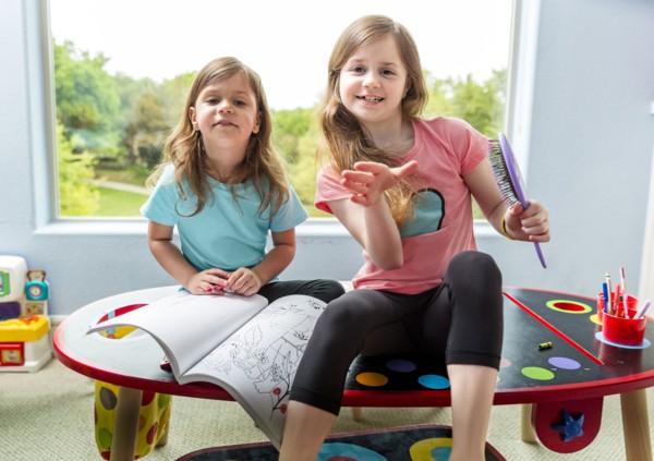 Caucasian sisters drawing at table in playroom