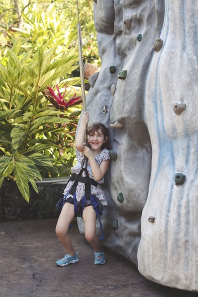 Caucasian girl climbing rock wall in harness