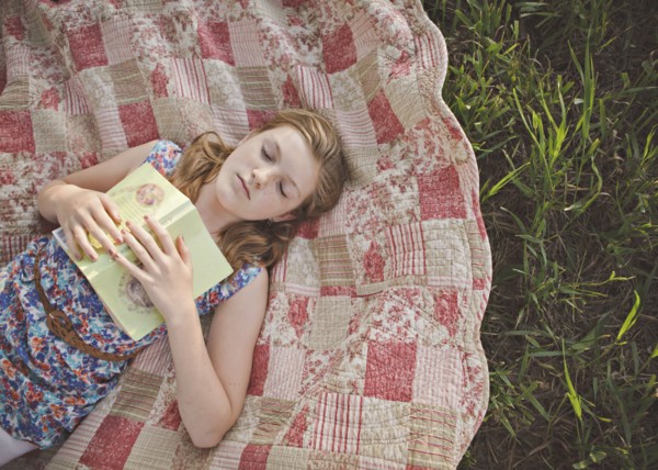 Caucasian girl sleeping with book on blanket