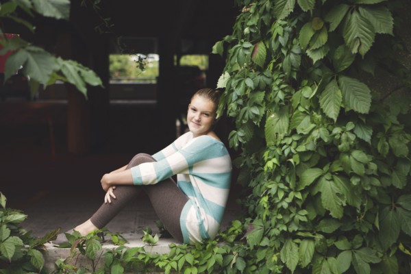 Caucasian teenage girl sitting at ivy wall