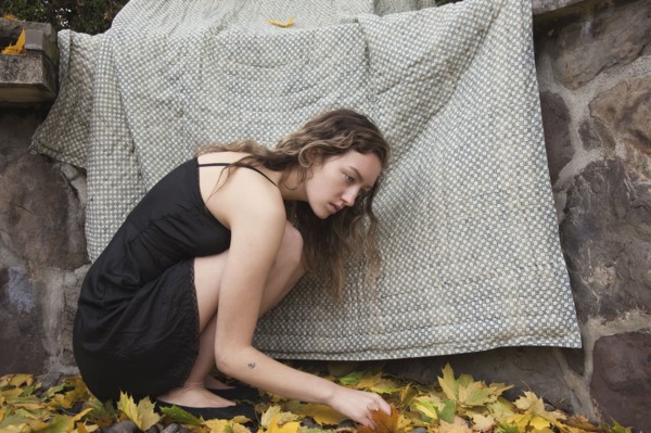 Woman crouching under blanket near stone wall