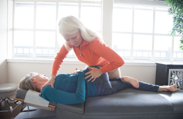 Caucasian chiropractor stretching back of client