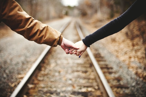 Close up of couple holding hands on railroad tracks