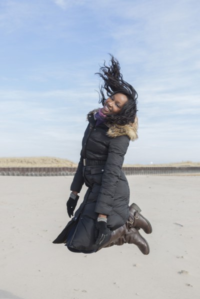 Woman in coat jumping for joy on beach