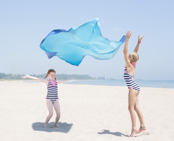 Caucasian girls playing with fabric on beach