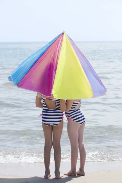 Caucasian girls under umbrella on beach