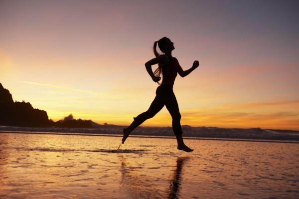 Silhouette of woman running on beach at sunset