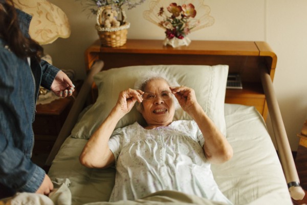 Granddaughter giving grandmother eyeglasses in bed