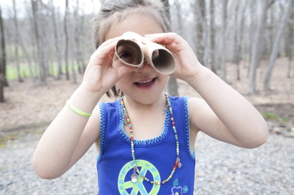 Caucasian girl playing with cardboard tubes in forest