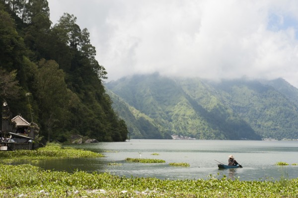 Fisherman rowing canoe on still rural lake