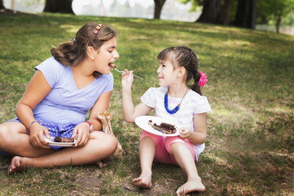Girl feeding sister cake at birthday party in park