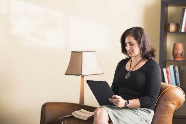 Hispanic woman sitting on armchair reading digital tablet
