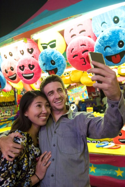 Smiling couple posing for cell phone selfie in amusement park