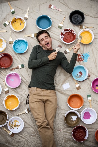 Man laying on tarp holding paintbrushes and singing