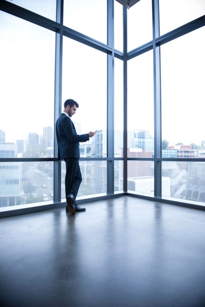 Hispanic businessman leaning on window texting on cell phone