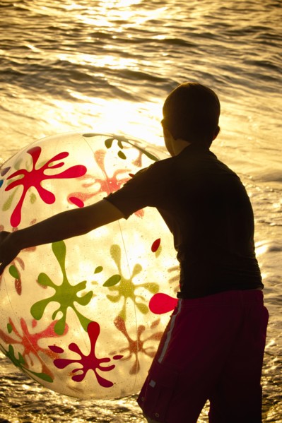 Silhouette of Caucasian boy holding beach ball at sunset