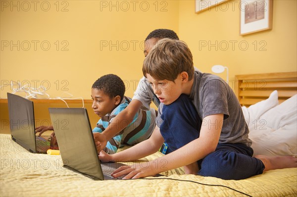 Boys sitting on bed using laptops