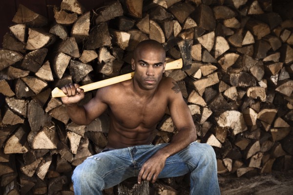 Bare chested African American man near woodpile holding ax